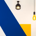 Suprematist abstract painting by Kazimir Malevich featuring a modern ceiling spot light and warm glowing pendant lamp. Minimalist composition of bold navy blue and vibrant yellow geometric shapes on a stark white background. Flat textures, sharp edges, avant-garde electrical concept. ##no humans##, ##no text##.