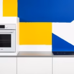 Suprematist abstract painting in the style of Kazimir Malevich featuring a built-in oven and an induction cooktop as central geometric forms. Minimalist avant-garde composition with bold navy blue and vibrant yellow rectangles, circles and dynamic diagonal lines on a stark white background. Flat matte textures, sharp clean edges, subtle electrical energy suggested through geometric rays and intersecting planes, representing a safe and compliant kitchen electrical installation. No humans, no text, no lettering, no watermark.