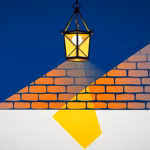 Suprematist abstract painting by Kazimir Malevich featuring a wrought-iron porch lantern casting warm geometric light beams across a brick and half-timbered wall. Minimalist composition of bold navy blue and vibrant yellow geometric shapes on a stark white background. Flat textures, sharp edges, avant-garde electrical concept. No humans, no text, no letters, no watermark, no text overlay.