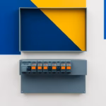 Suprematist abstract painting by Kazimir Malevich featuring an open electrical consumer unit with a row of differential circuit breakers mounted on a DIN rail. Minimalist composition of bold navy blue and vibrant yellow geometric shapes on a stark white background. Flat textures, sharp edges, avant-garde electrical concept. No humans, no text.