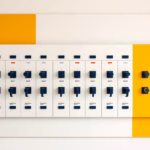 Suprematist abstract painting inspired by Kazimir Malevich showing a wall-mounted electrical distribution board with oversized lever switches arranged in neat labelled rows. Minimalist composition of bold navy blue and vibrant yellow geometric shapes on a stark white background. Flat matte textures, sharp crisp edges, avant-garde electrical concept, no humans, no text, no letters, no numbers, no logos.